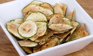 Un bol blanc rempli de chips de courgette croustillantes, assaisonnées d'épices.
