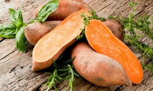 Patates douces coupées, prêtes pour la cuisson à l'eau bouillante, garnies de basilic et de thym frais sur fond de bois rustique.