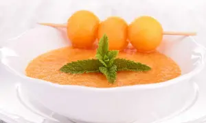 Un bol de gaspacho de melon, garni de feuilles de menthe et de billes de melon sur une brochette. Rafraîchissant et coloré.
