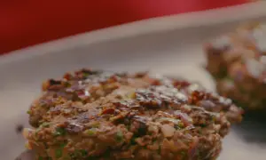 Deux steaks hachés plancha, grillés à la perfection, avec des morceaux d'oignon rouge et de persil.