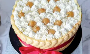 Magnifique recette charlotte : une mousse aérienne, des marrons glacés et une touche d'or comestible, le tout entouré d'une belle robe de biscuits cuillère et d'un ruban rouge.