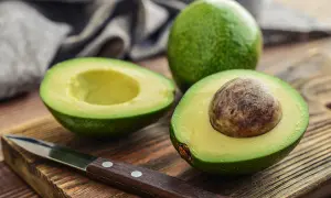 Un avocat coupé en deux sur une planche en bois, prêt à être préparé. Astuce pour empêcher un avocat de noircir sans citron.