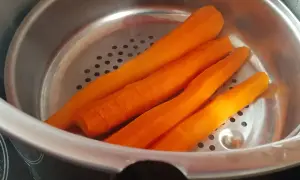 Carottes pelées prêtes pour la cuisson à la cocotte minute. Elles sont disposées dans un panier vapeur métallique.