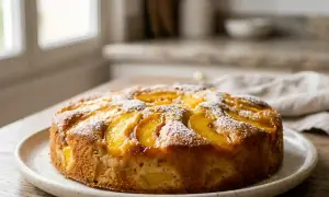 Gâteau aux pêches doré, saupoudré de sucre glace, prêt à être dégusté.