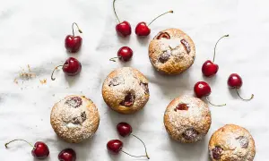 Financiers aux cerises saupoudrés de sucre glace, disposés avec des cerises fraîches sur un tissu blanc.