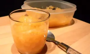Compote pomme poire vanille dans un verre, avec une cuillère et un récipient en arrière-plan.