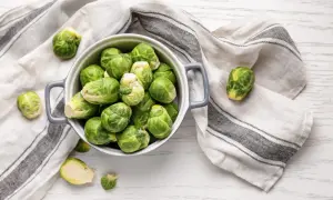 Un bol gris rempli de choux de Bruxelles frais, prêts pour la cuisson. Quelques choux sont éparpillés autour, sur une serviette rayée.