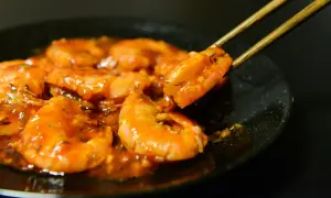 Gambas plancha enrobées d'une sauce orangée, une crevette est saisie par des baguettes.