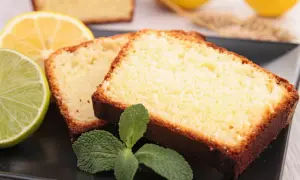 Tranches de gâteau moelleux au citron grand-mère, garnies de menthe fraîche, avec des citrons et une lime en arrière-plan.