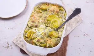 Plat gratiné de ravioles aux poireaux, une recette de Laurent Mariotte, servi dans un plat blanc avec une cuillère.