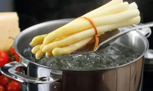 Un bouquet d'asperges blanches est plongé dans l'eau bouillante pour une cuisson parfaite.