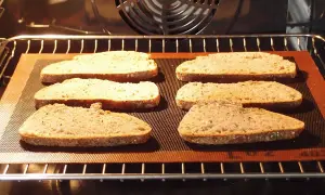 Six tranches de pain de campagne, prêtes pour la décongélation pain four, sur une plaque en silicone dans un four chaud.