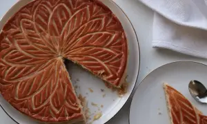 Une galette aux amandes dorée, décorée de motifs feuillus, est servie sur une assiette. Une part est déjà coupée.