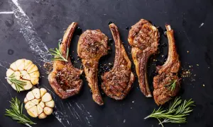 Quatre côtelettes d'agneau grillées, assaisonnées et garnies de romarin, avec des têtes d'ail rôties. La cuisson côtelette agneau parfaite.