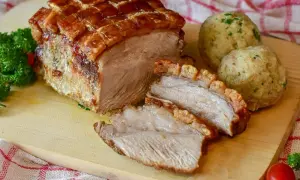 Rôti de porc croustillant, coupé en tranches, servi avec des boules de pain et du persil. Le temps de cuisson du rôti de porc est parfait.