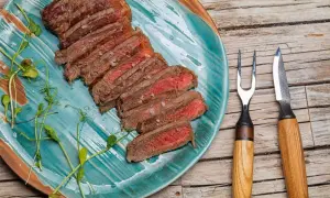 Tranches d'onglet de bœuf saignant, parsemées de gros sel, sur une assiette turquoise. Une fourchette et un couteau à steak sont à droite.