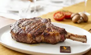 Un magnifique côte de bœuf, prêt à être dégusté. Grillé à la perfection, il attend patiemment sur une assiette blanche, accompagné de tomates et de champignons.