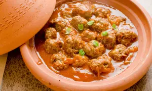 Un plat de tajine kefta, des boulettes de viande mijotées dans une sauce tomate épicée, garni de feuilles de menthe fraîche.