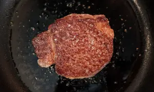 Un beau morceau de Black Angus en cuisson dans une poêle, avec des cristaux de sel qui fondent.