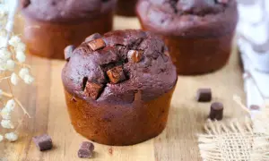 Gros plan sur un muffin banane chocolat moelleux, parsemé de pépites de chocolat, sur une planche en bois.