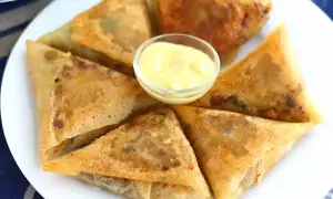 Assiette de samoussas boeuf dorés et croustillants, servis avec une sauce jaune crémeuse.