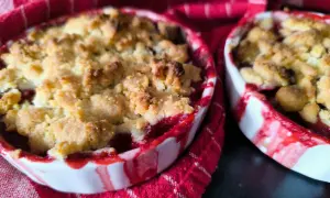 Deux petits ramequins de crumble aux quetsches, aux bords rouges et blancs, sur un torchon à rayures rouges.