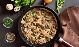 Une poêle remplie d'escalope à la crème et de champignons, garnie de persil frais et d'une branche de romarin.