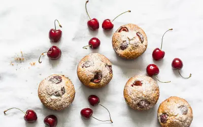 Financiers aux cerises saupoudrés de sucre glace, disposés avec des cerises fraîches sur un tissu blanc.