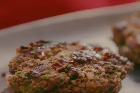 Deux steaks hachés plancha, grillés à la perfection, avec des morceaux d'oignon rouge et de persil.