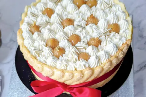 Magnifique recette charlotte : une mousse aérienne, des marrons glacés et une touche d'or comestible, le tout entouré d'une belle robe de biscuits cuillère et d'un ruban rouge.