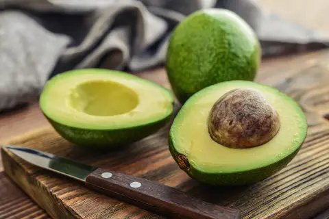 Un avocat coupé en deux sur une planche en bois, prêt à être préparé. Astuce pour empêcher un avocat de noircir sans citron.