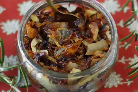 Un bocal rempli de confit d'oignon caramélisé, prêt à être dégusté. Une cuillère dorée y est plongée.