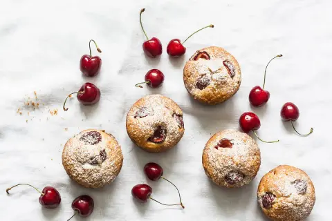 Financiers aux cerises saupoudrés de sucre glace, disposés avec des cerises fraîches sur un tissu blanc.