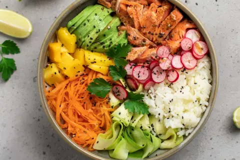 Un bol coloré avec saumon, avocat, mangue, carottes râpées, radis, courgette et riz blanc. Parfait pour des menus semaine famille équilibrés et savoureux.