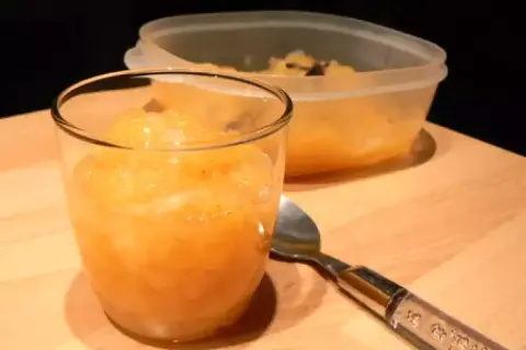 Compote pomme poire vanille dans un verre, avec une cuillère et un récipient en arrière-plan.