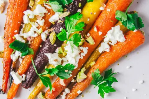 Carottes multicolores rôties, parsemées de feta émiettée, de pistaches concassées et de persil frais. Un délice pour la cuisson carottes.