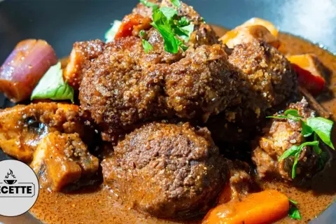 Un plat réconfortant de boeuf miroton recette, avec des morceaux de viande tendres mijotés dans une sauce savoureuse, accompagnés de carottes et d'oignons.