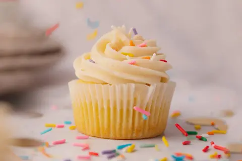 Un cupcake vanille avec glaçage crémeux et vermicelles colorés tombant. Une recette facile pour un goûter gourmand.