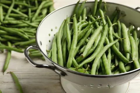 Haricots verts frais et humides dans une passoire, prêts pour la cuisson. Une belle récolte pour un plat sain.
