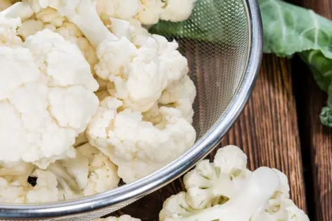 Chou-fleur frais coupé en bouquets dans une passoire, prêt pour la cuisson. Eau froide ou chaude, le choix dépend de la recette.