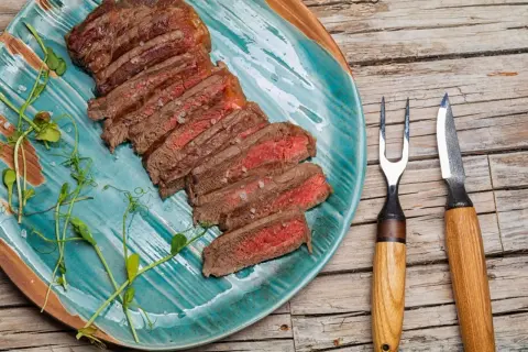 Tranches d'onglet de bœuf saignant, parsemées de gros sel, sur une assiette turquoise. Une fourchette et un couteau à steak sont à droite.