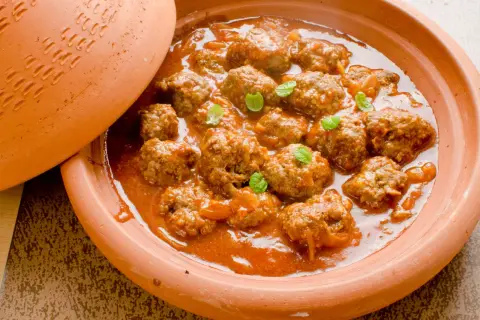 Un plat de tajine kefta, des boulettes de viande mijotées dans une sauce tomate épicée, garni de feuilles de menthe fraîche.