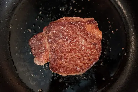 Un beau morceau de Black Angus en cuisson dans une poêle, avec des cristaux de sel qui fondent.