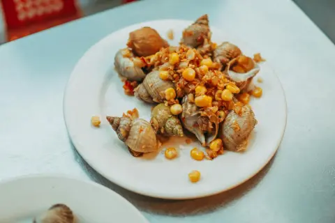 Bulots cuisinés avec maïs et épices, prêts à être dégustés après leur temps de cuisson au court-bouillon.