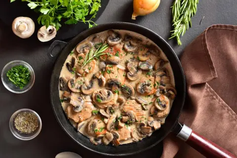 Une poêle remplie d'escalope à la crème et de champignons, garnie de persil frais et d'une branche de romarin.