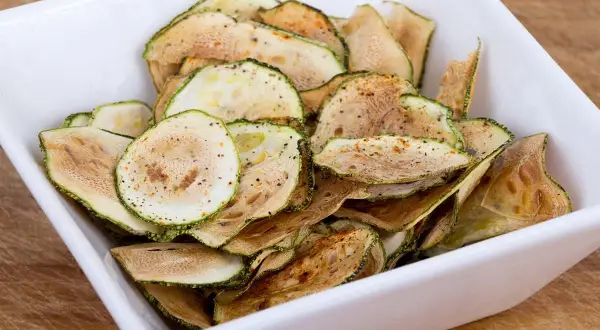 Un bol blanc rempli de chips de courgette croustillantes, assaisonnées d'épices.