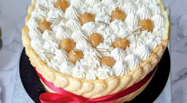 Magnifique recette charlotte : une mousse aérienne, des marrons glacés et une touche d'or comestible, le tout entouré d'une belle robe de biscuits cuillère et d'un ruban rouge.