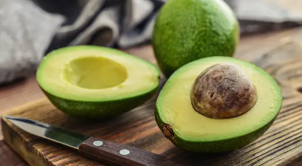 Un avocat coupé en deux sur une planche en bois, prêt à être préparé. Astuce pour empêcher un avocat de noircir sans citron.