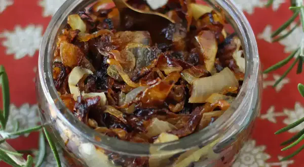 Un bocal rempli de confit d'oignon caramélisé, prêt à être dégusté. Une cuillère dorée y est plongée.