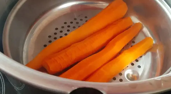 Carottes pelées prêtes pour la cuisson à la cocotte minute. Elles sont disposées dans un panier vapeur métallique.